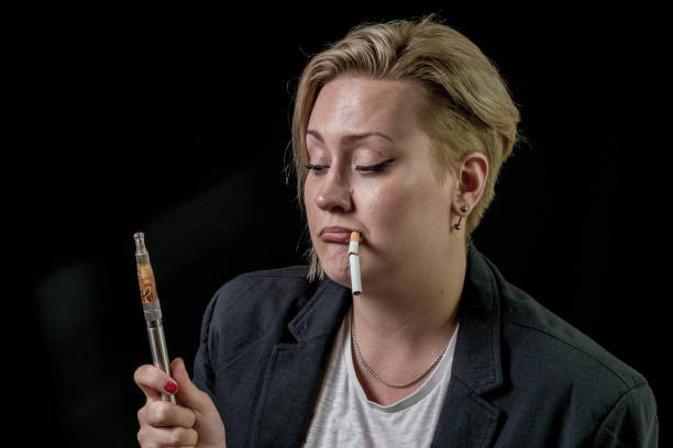 여자는 그녀의 치아 사이 담배 담배를 들고 vaping 기화 기에 대 한 질문 - lesbian women thinking black 뉴스 사진 이미지