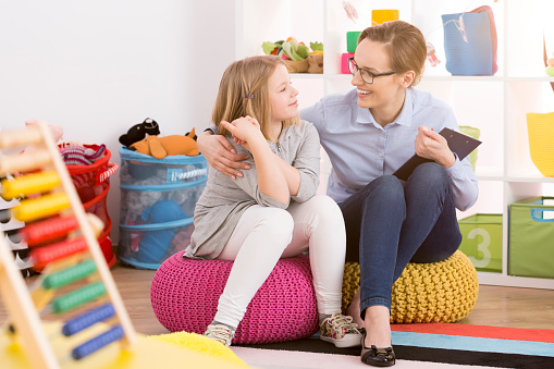 Young speech therapist working with child in colorful educational playroom