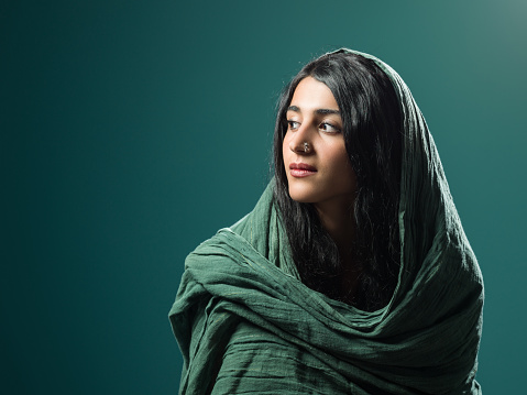 Head and shoulder portrait of beautiful adult woman wearing green headscarf.She has brown eyes, long black hair and nose ring.The background is green color.Shot in studio with medium format camera.