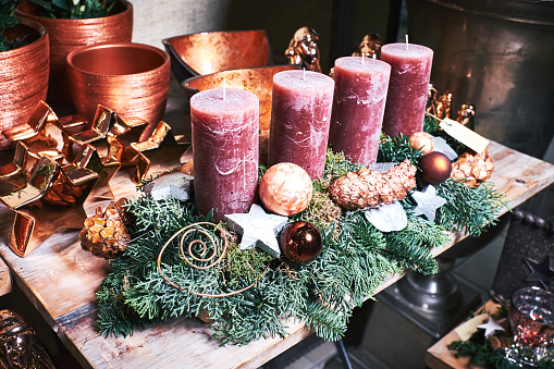 Vibrant red poinsettias & Christmas ornaments or baubles surround a burning red pillar candle on black background. Horizontal Christmas image.