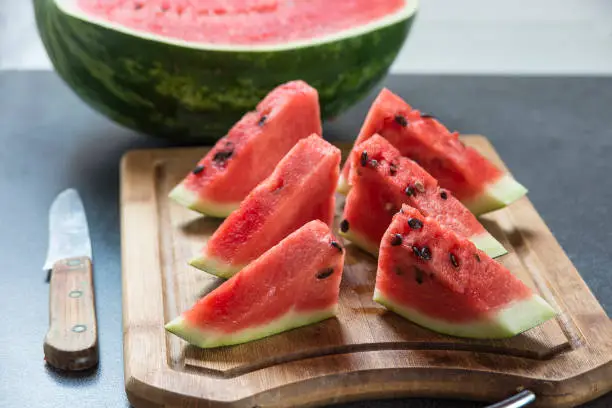 Six watermelon slices on wooden board with knife