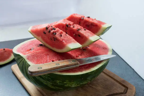 Three watermelon slices sit on the half of watermelon with knife