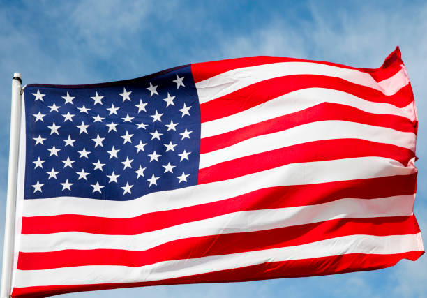 istock American Flag Against a Blue Cloud Filled Sky 820741596