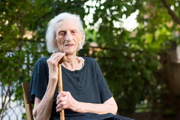 Senior woman sitting with a walking cane outdoors