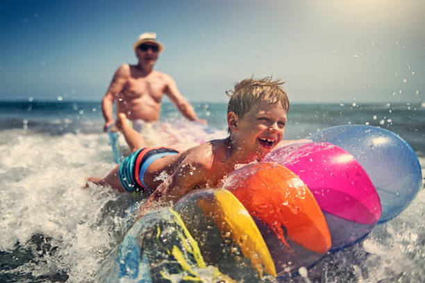 little boy with grandfather playing in sea waves - inflatable raft nautical vessel sea inflatable imagens e fotografias de stock