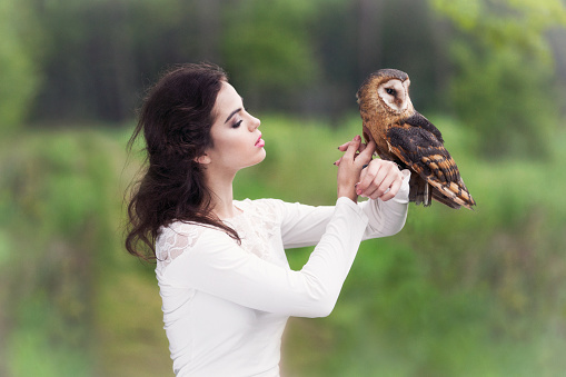 Portrait of a beautiful caucasian young woman posing with a barn owl in a forest.