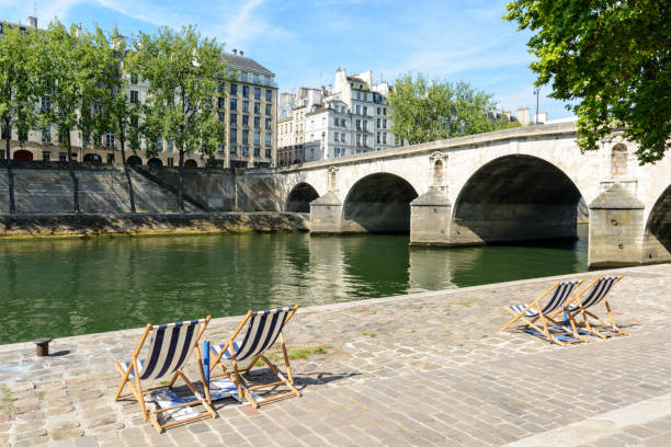 Deck chairs in the sun on the bank of the river Seine Blue and white striped deck chairs in the sun on the bank of the river Seine with typical parisian bridge and buildings in the background. quayside photos stock pictures, royalty-free photos & images