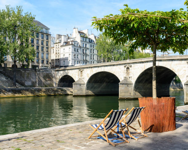 Two deck chairs in the sun in front of the river Seine.