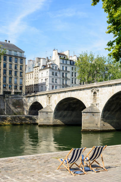 istock Two deck chairs in the sun in front of the river Seine. 820775904