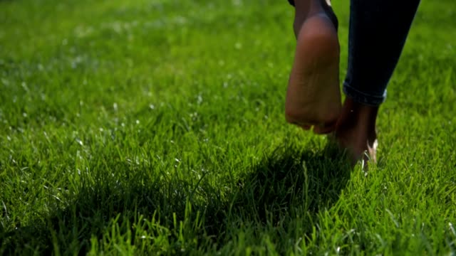 Close up of barefooted young girl walking on grass