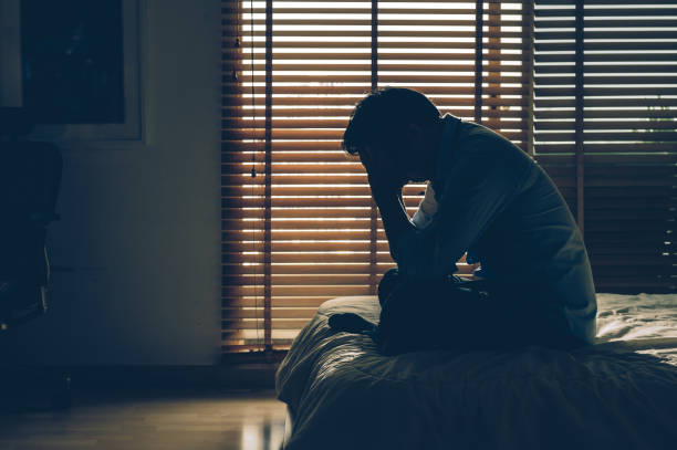 empresário triste sentado cabeça nas mãos em cima da cama no quarto escuro com pouca luz ambiente, conceito dramático, vintage de tom de cor - estado médico - fotografias e filmes do acervo