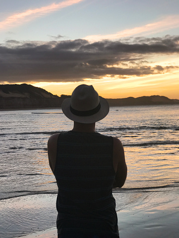 Young athletic backpacker tourist man looking the Atlantic Ocean wearing a Panama Hat in a sunset afternoon at Jericoacoara National Park, Brazil.