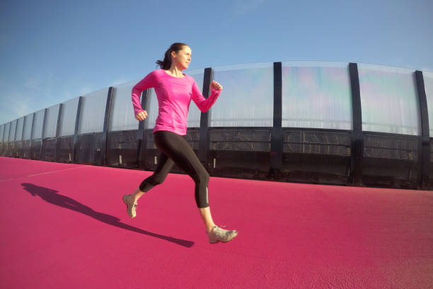 Young woman (age 30) running on a bright pink cycleway road in Auckland, New Zealand. Real people. Copy space.