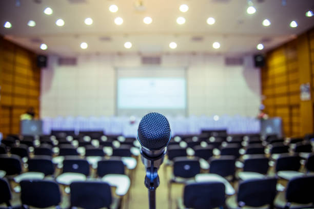 Microphone over the Abstract blurred photo of conference hall or seminar room background Microphone over the Abstract blurred photo of conference hall or seminar room background auditorium photos stock pictures, royalty-free photos & images