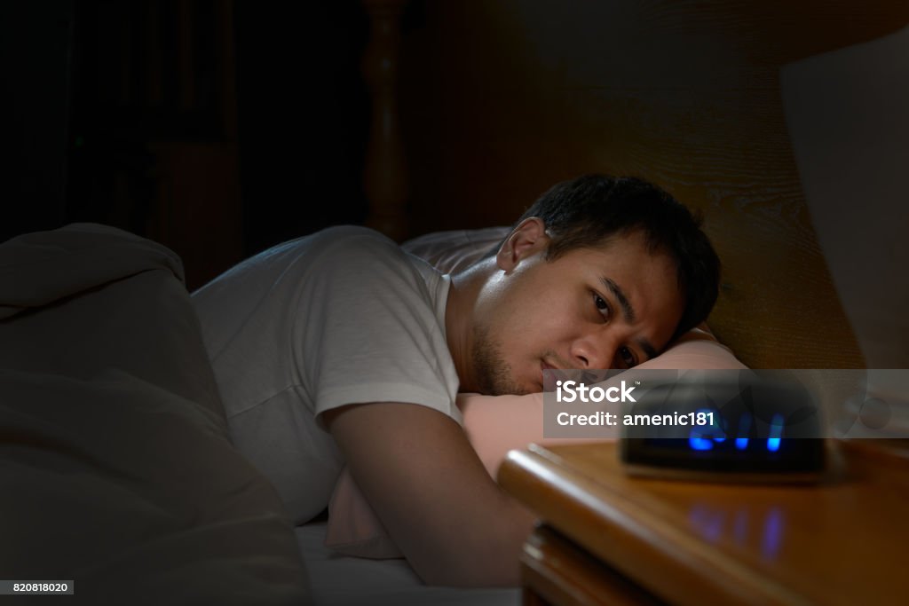 Depressed man suffering from insomnia lying in bed Insomnia Stock Photo