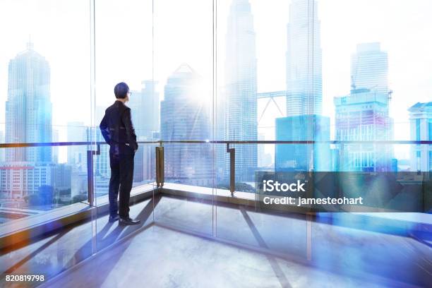 Young Businessman Looking Out The City In The Office Morning Scene Stock Photo - Download Image Now