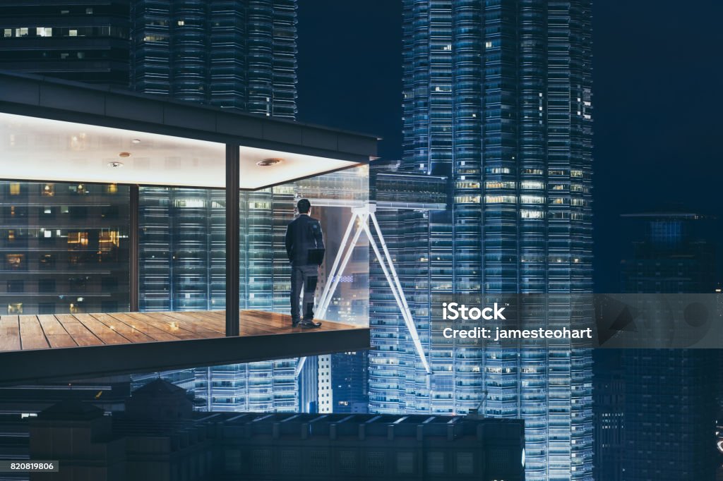 Businessman in an modern sky office by night with beautiful city skyline view . Looking Through Window Stock Photo