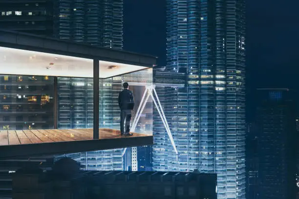 Photo of Businessman in an modern sky office by night with beautiful city skyline view .