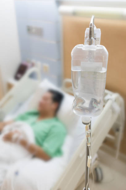 Blurred image of male patient lying on hospital bed, with saline solution bag as foreground. stock photo