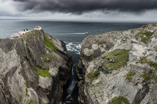 Ferry crossing rocky headland, with storm clouds approaching Ferry crossing rocky headland of Mizen Head, County Cork, Ireland, with dark storm clouds approaching. mizen head stock pictures, royalty-free photos & images