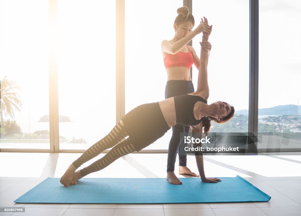 Yoga teachers or yoga trainer are teaching Side Plank Pose and  help to adjust the posture and balance of the body to older women's beginner Yoga . Yoga teachers or yoga trainer are teaching Side Plank Pose and  help to adjust the posture and balance of the body to older women's beginner Yoga Teaching Stock Photo