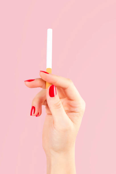 Female hand holding cigarette. Female hand holding cigarette isolated on pink background. Feminine tobacco abuse. red nail polish stock pictures, royalty-free photos & images