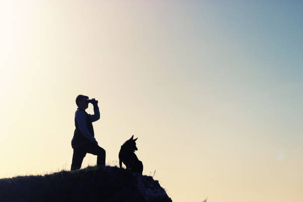 man and his dog stand on mountain peak. solder explorer concept