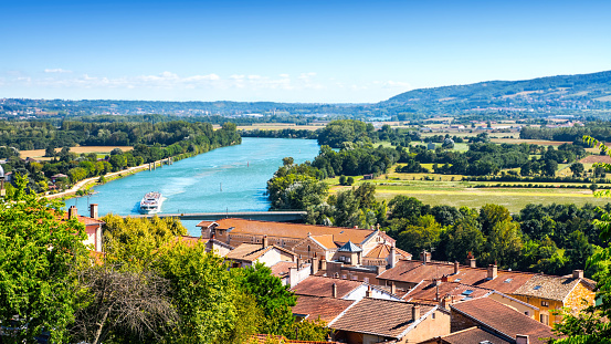 High angle view of trees, fileds, house roof, Saone river and Beaujolais hills in background of Trevoux beautiful town landscape in summer season with a bright sunlight. This pretty medieval town is located in Ain, Auvergne-Rhone-Alpes region in France near Lyon city along Saone river.