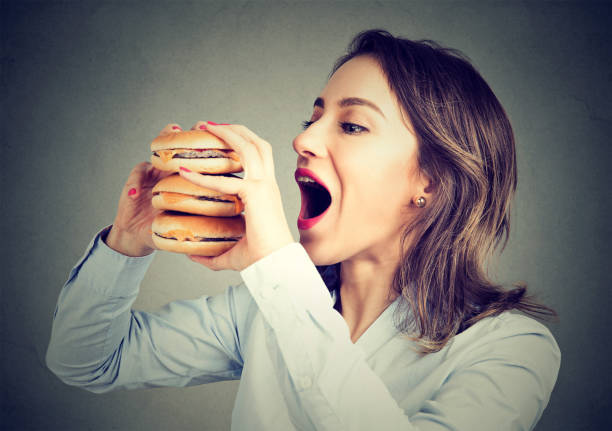 Woman eating craving a tasty double burger Woman eating craving a tasty double burger greed photos stock pictures, royalty-free photos & images