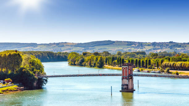 High angle view landscape of Trevoux town footbridge crossing the Saone river near Lyon city scenic in France High angle view of trees and field of Trevoux city beautiful old footbridge, crossing Saone river in Beaujolais region with lush foliage hills in background during a sunny summer day. This pretty medieval town is located in Ain, Auvergne-Rhone-Alpes region in France near Lyon city along Saone river. beaujolais region stock pictures, royalty-free photos & images