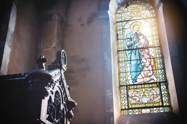 Photo of Close-up of beautiful christian stained glass transparent window from french church of Trevoux town indoor with sunlight