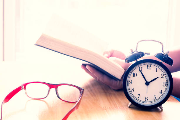 istock Reading book on table. focus on retro alarm clock. Time to read concept. 820863490