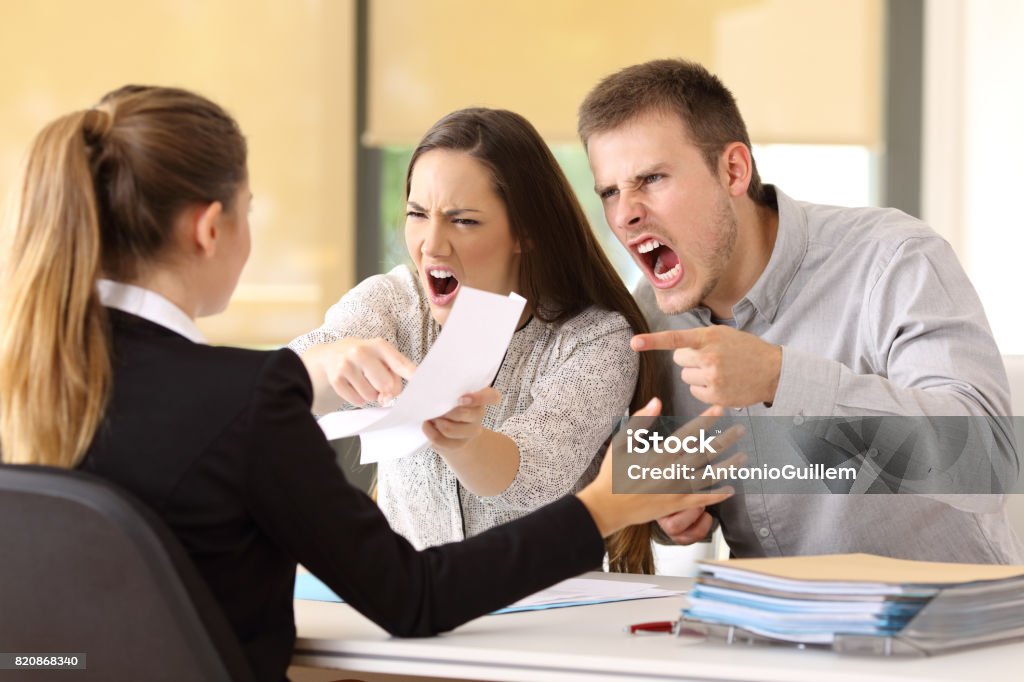 Angry couple claiming at office Angry couple claiming and shouting to an office worker Customer Stock Photo