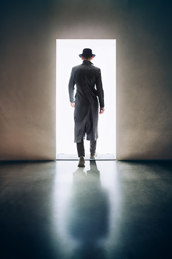 Man silhouette walking away in the light of opening door in dark room. escape concept