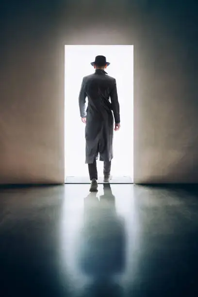 Photo of Man silhouette walking away in the light of opening door in dark room