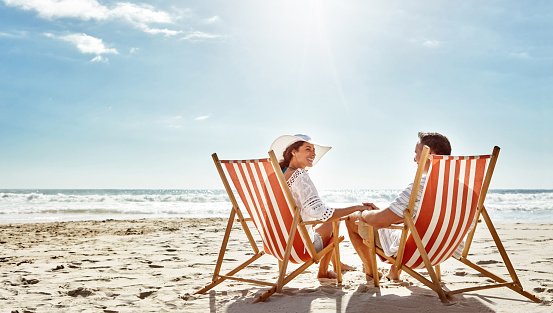 Shot of a mature couple relaxing together on deck chairs at the beach