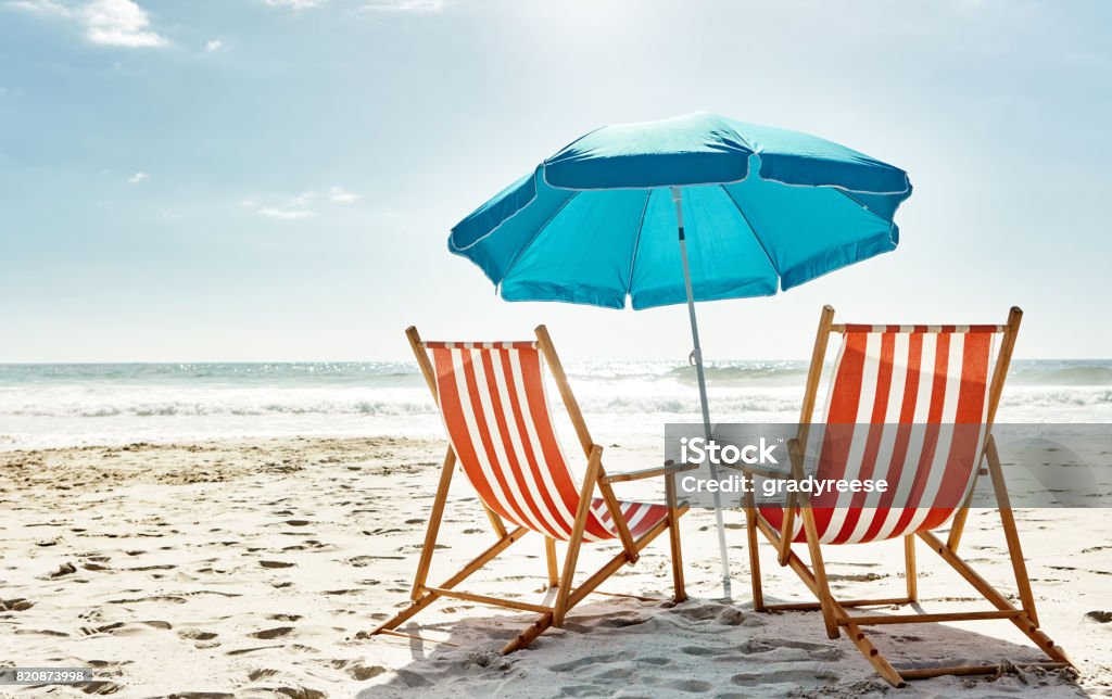 Get some summer in your life Still life shot of two deck chairs under an umbrella on the beach Summer Stock Photo