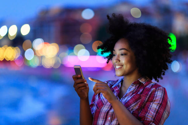 привлекательная женщина с помощью смартфона ночью на улице - people traveling flash стоковые фото и изображения