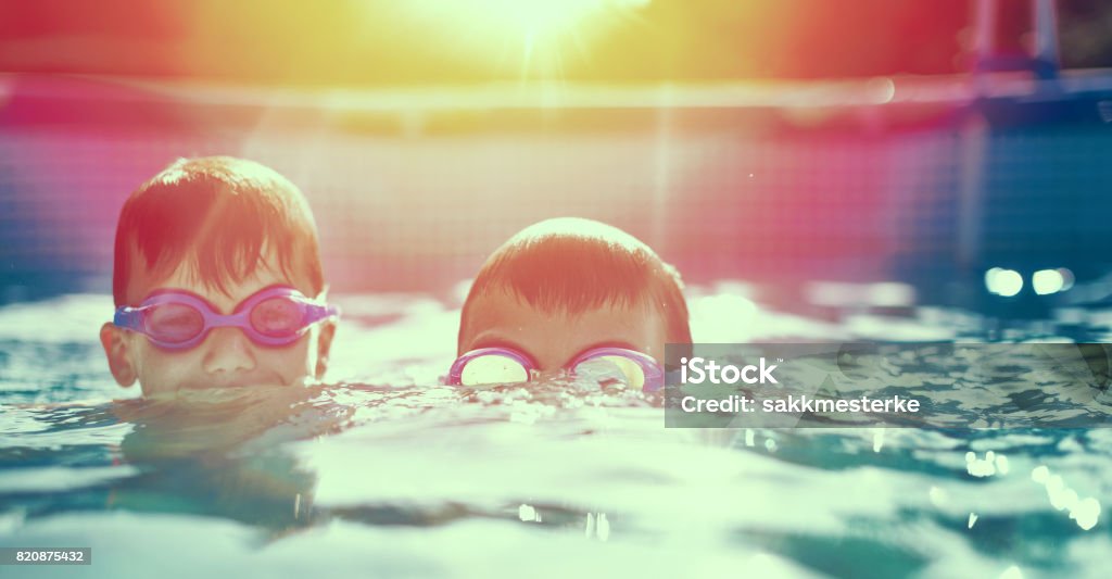 Deux petits enfants dans des lunettes de natation dans la piscine au coucher du soleil - Photo de Piscine libre de droits