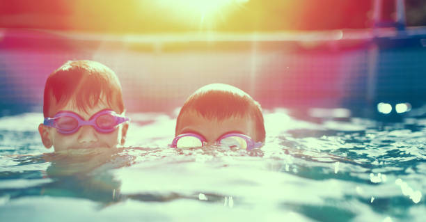 Two little kids in goggles swimming in pool at sunset Two little kids in goggles swimming in pool at vintage sunset vintage pool stock pictures, royalty-free photos & images