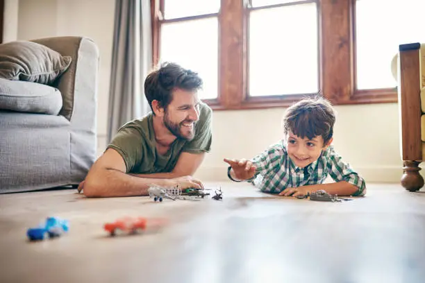 Shot of a little boy and his father playing toy cars at home
