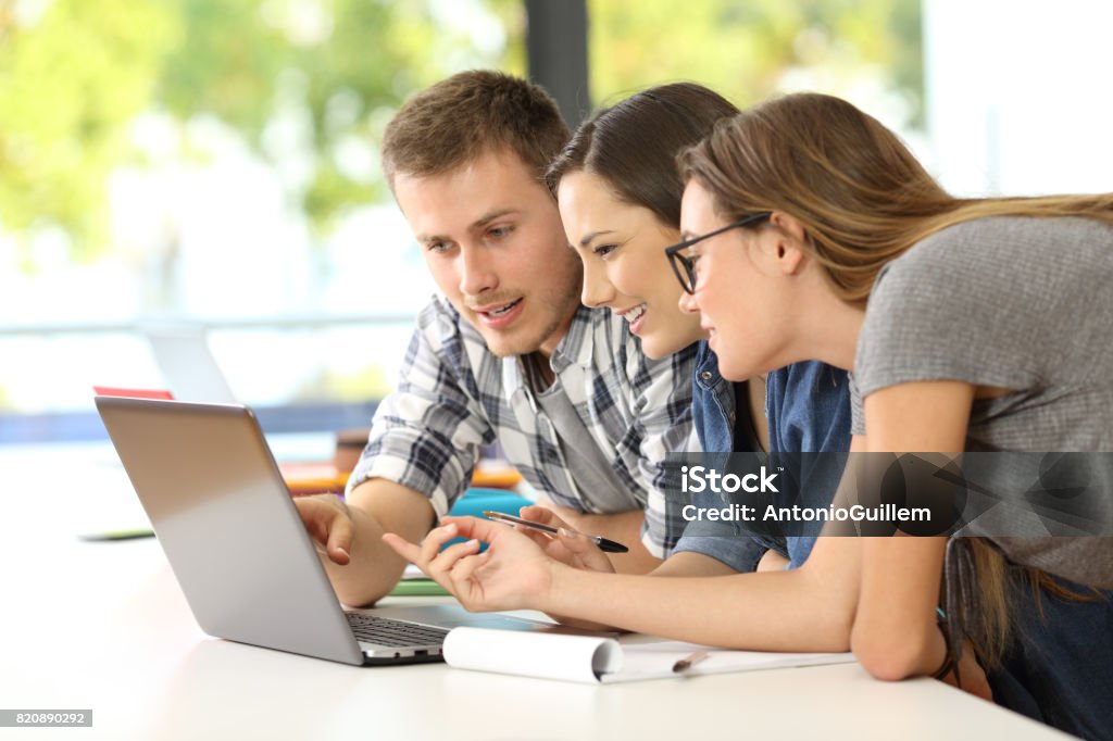 Students learning together on line in a classroom Three students learning together on line with a laptop in a classroom University Student Stock Photo
