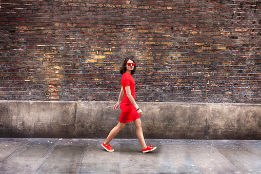 Woman in red dress walking in front of brick wall