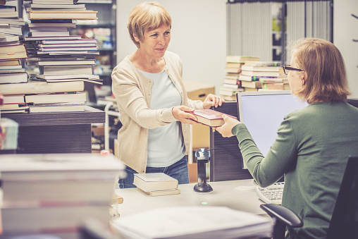 Book rental, librarian and an adult woman with books. Europe. Nikon. No logo - titles and writings on books all removed, covered or blurred.