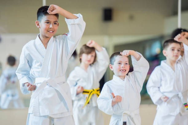 Blocking A multi-ethnic group of children are indoors at a Taekwondo academy. They are wearing martial arts clothing. They are practicing their techniques and smiling. defending sport photos stock pictures, royalty-free photos & images