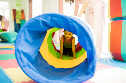 Little kid playing and crawling through a tunnel in an obstacle course at a children physical therapy center