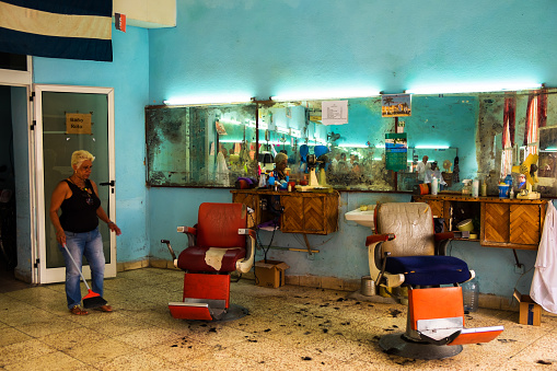 Woman cleaning hairs on the floor in a barber shop in Avana, Cuba