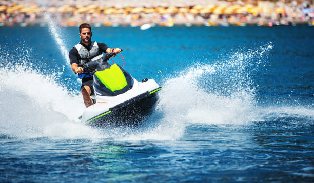 Jet skiing. Closeup front view of a young man riding a jet ski on a sunny summer day at open sea. He's wearing swimming suit and a life jacket. neoprene photos stock pictures, royalty-free photos & images