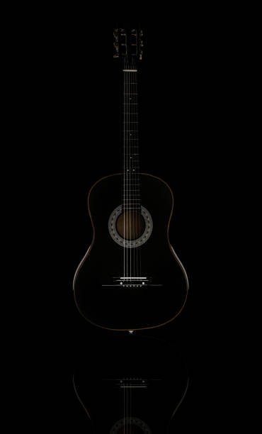 Black acoustic guitar isolated on black reflective surface, standing vertical