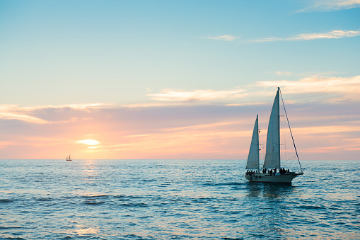 This is a horizontal, color photograph shot in travel destination, Puerto Vallarta, Mexico. A sailboat moves through the Pacific Ocean at sunset as it drives back toward the docks.